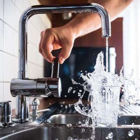 Man turning on faucet with water splashing out of glass